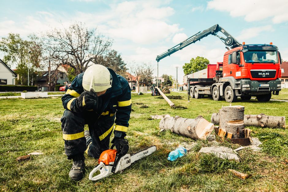 Arborist in safety gear using chainsaw beside truck with crane in an outdoor setting.