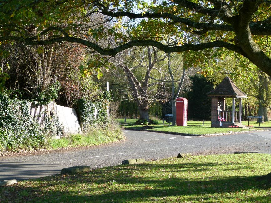 A serene countryside setting featuring a classic red phone box and lush foliage under a large tree.